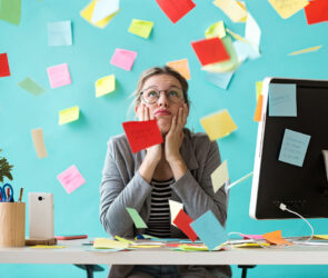 Overwhelmed business owner resting her chin in her hands at a desk surrounded by scattered sticky notes