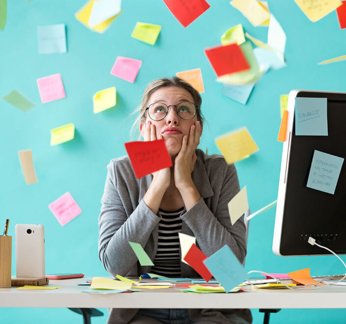Overwhelmed business owner resting her chin in her hands at a desk surrounded by scattered sticky notes