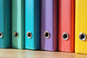 Row of colorful binders standing upright on a wooden shelf, representing written small business policies