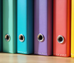 Row of colorful binders standing upright on a wooden shelf, representing written small business policies
