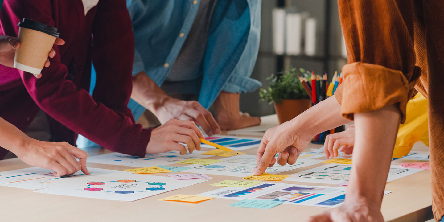 Several people leaning over a table together, sorting colorful sticky notes and printed plans