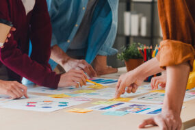 Several people leaning over a table together, sorting colorful sticky notes and printed plans