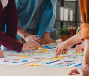 Several people leaning over a table together, sorting colorful sticky notes and printed plans