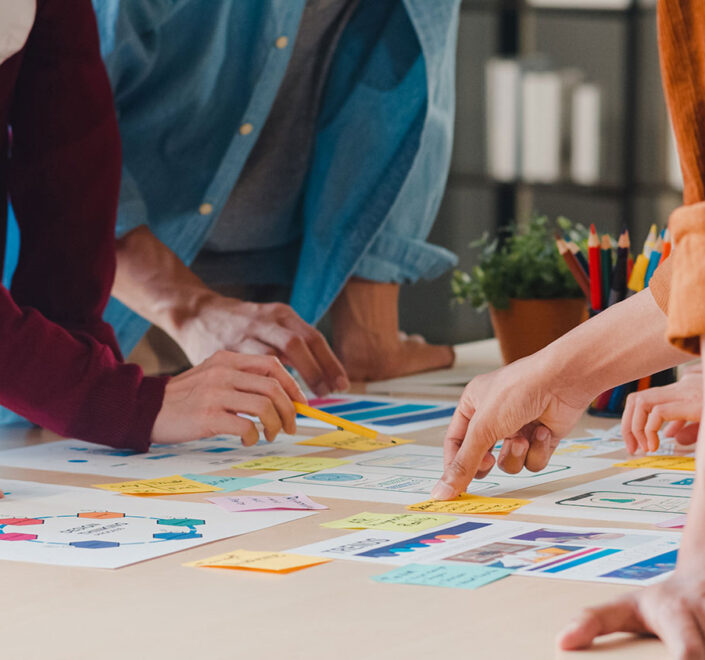 Several people leaning over a table together, sorting colorful sticky notes and printed plans
