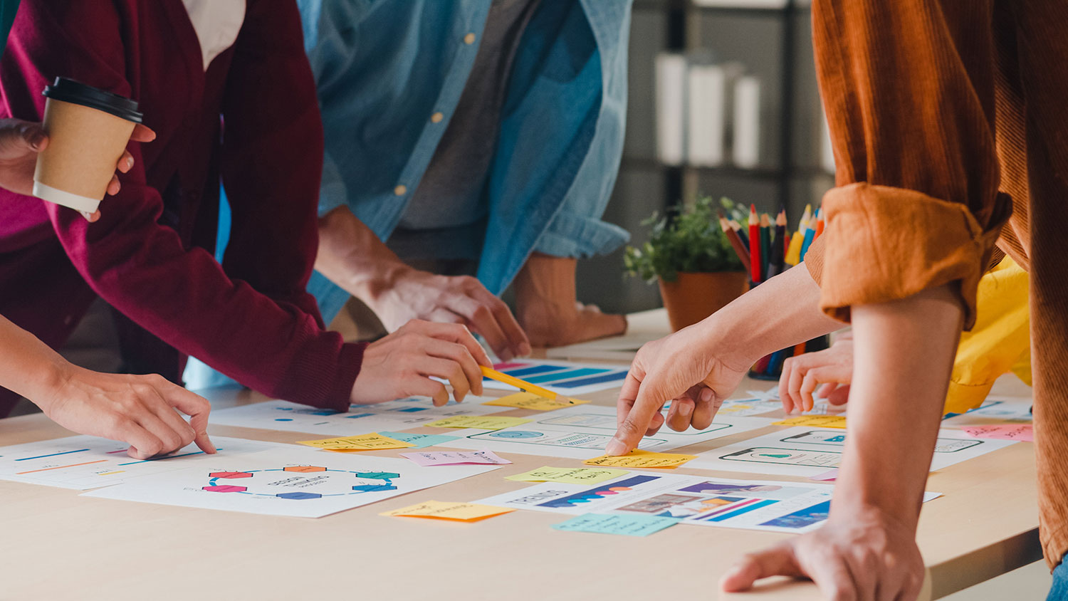 Several people leaning over a table together, sorting colorful sticky notes and printed plans