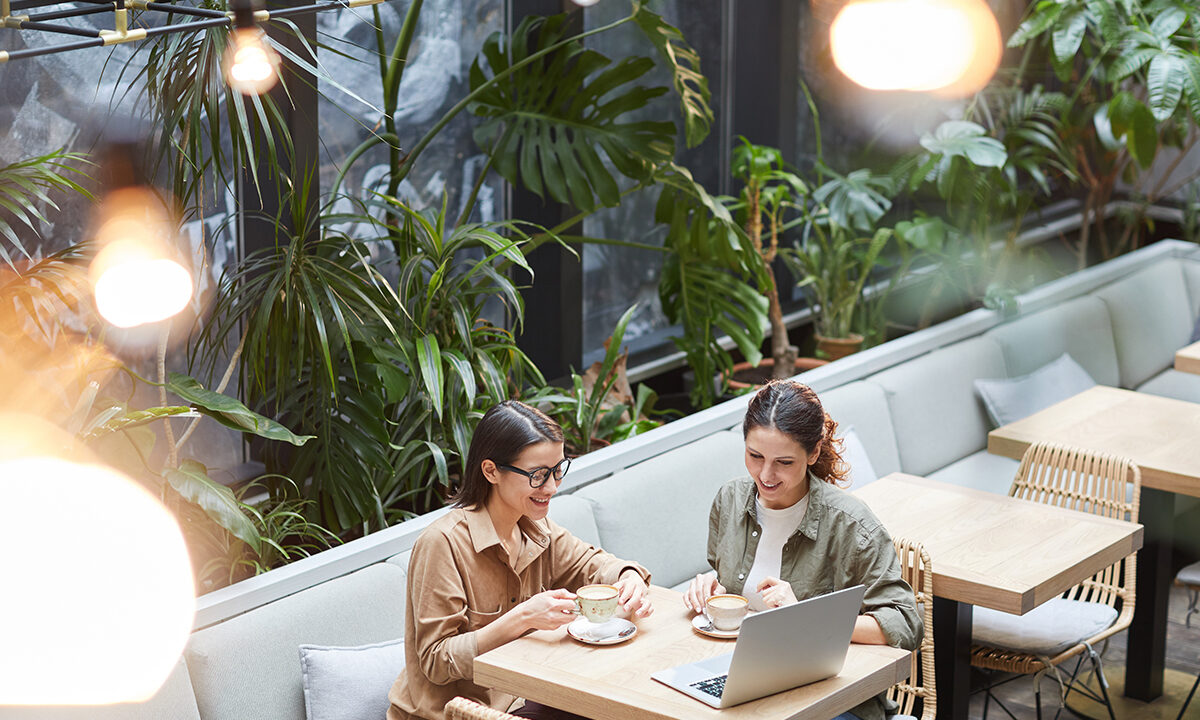 Two business owners talking over coffee and a laptop at a plant-filled cafe table