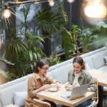 Two business owners talking over coffee and a laptop at a plant-filled cafe table