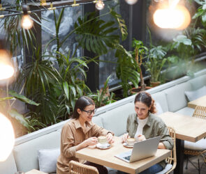 Two business owners talking over coffee and a laptop at a plant-filled cafe table