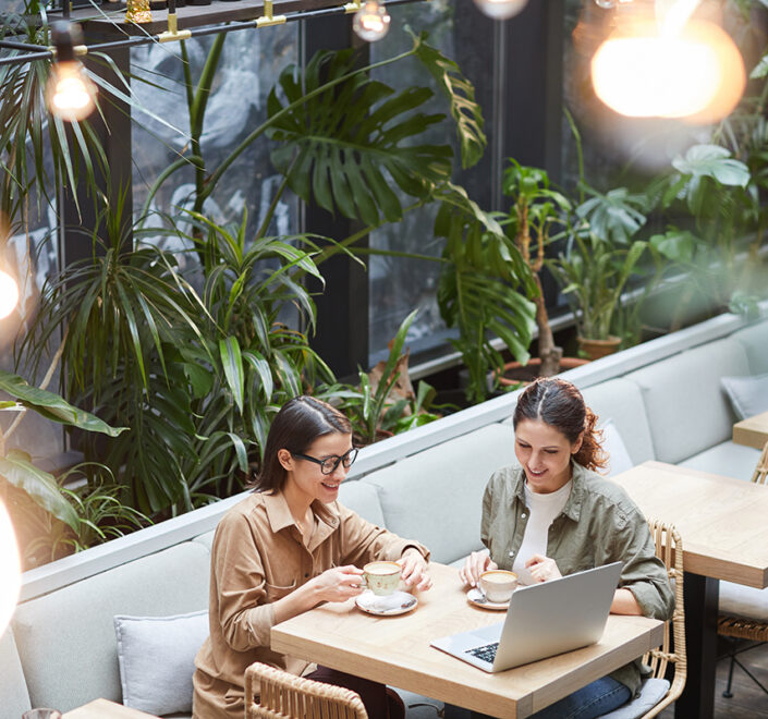 Two business owners talking over coffee and a laptop at a plant-filled cafe table