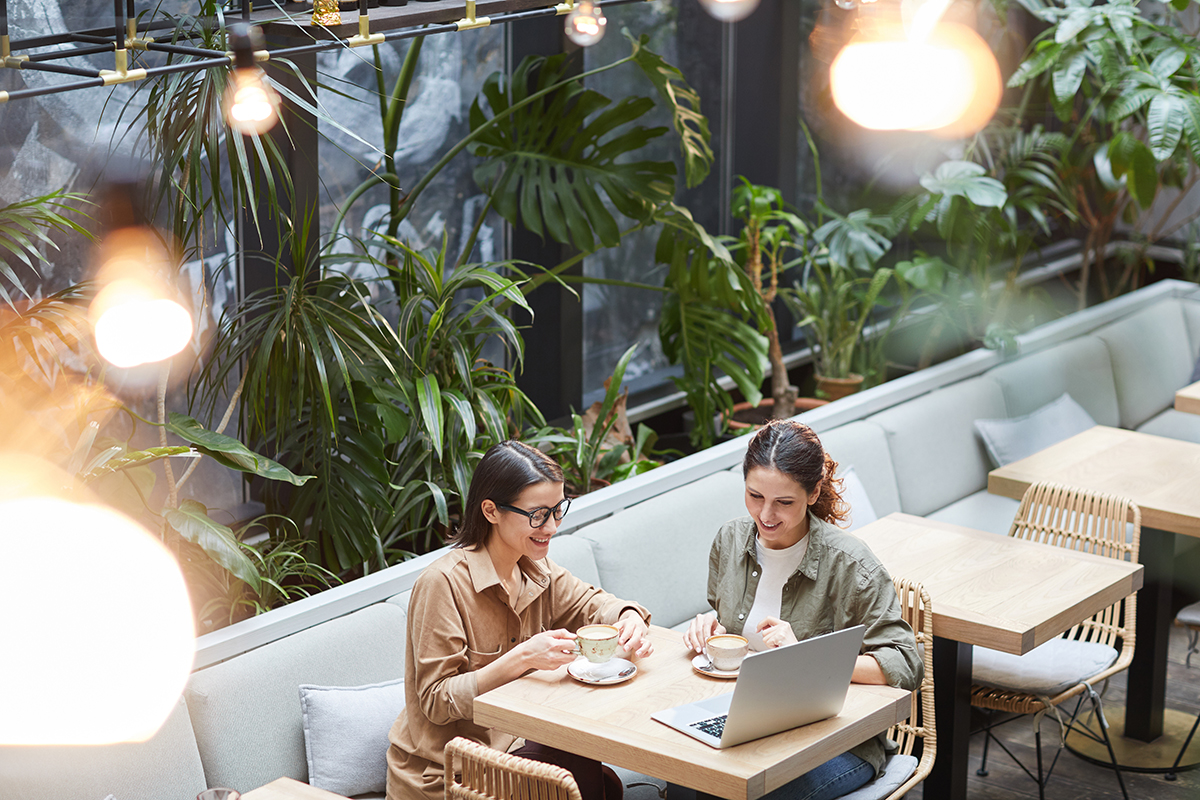Two business owners talking over coffee and a laptop at a plant-filled cafe table
