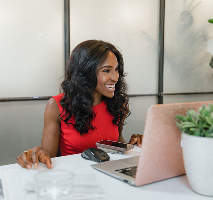 Consultant working at a laptop at a white desk with client paperwork spread beside her