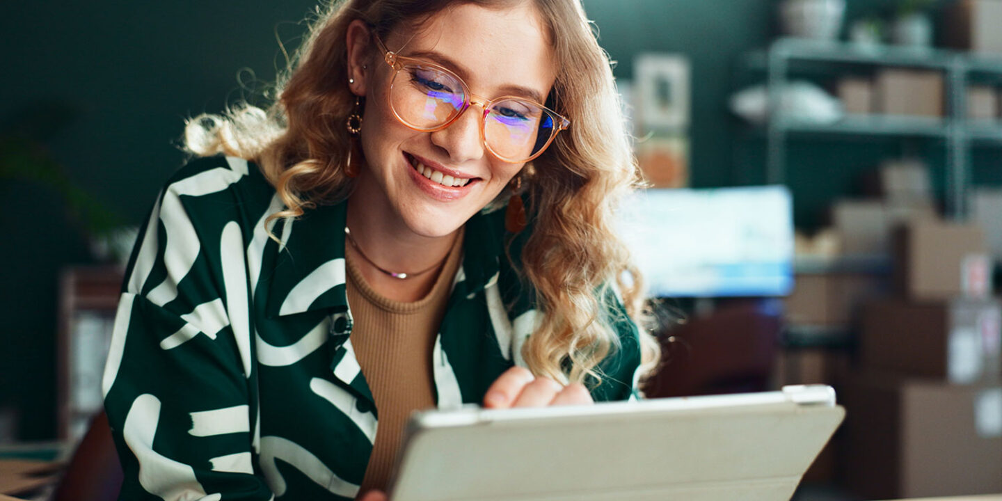 Smiling woman in glasses reading a message on her tablet in a small business workspace