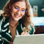 Smiling woman in glasses reading a message on her tablet in a small business workspace