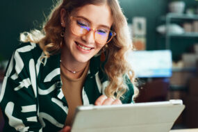 Smiling woman in glasses reading a message on her tablet in a small business workspace