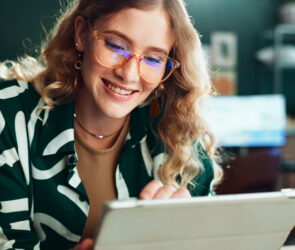 Smiling woman in glasses reading a message on her tablet in a small business workspace
