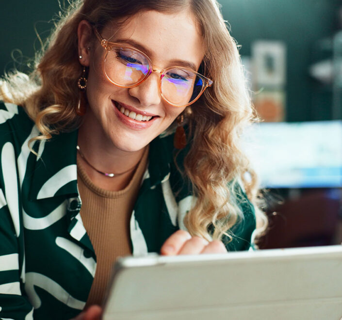 Smiling woman in glasses reading a message on her tablet in a small business workspace