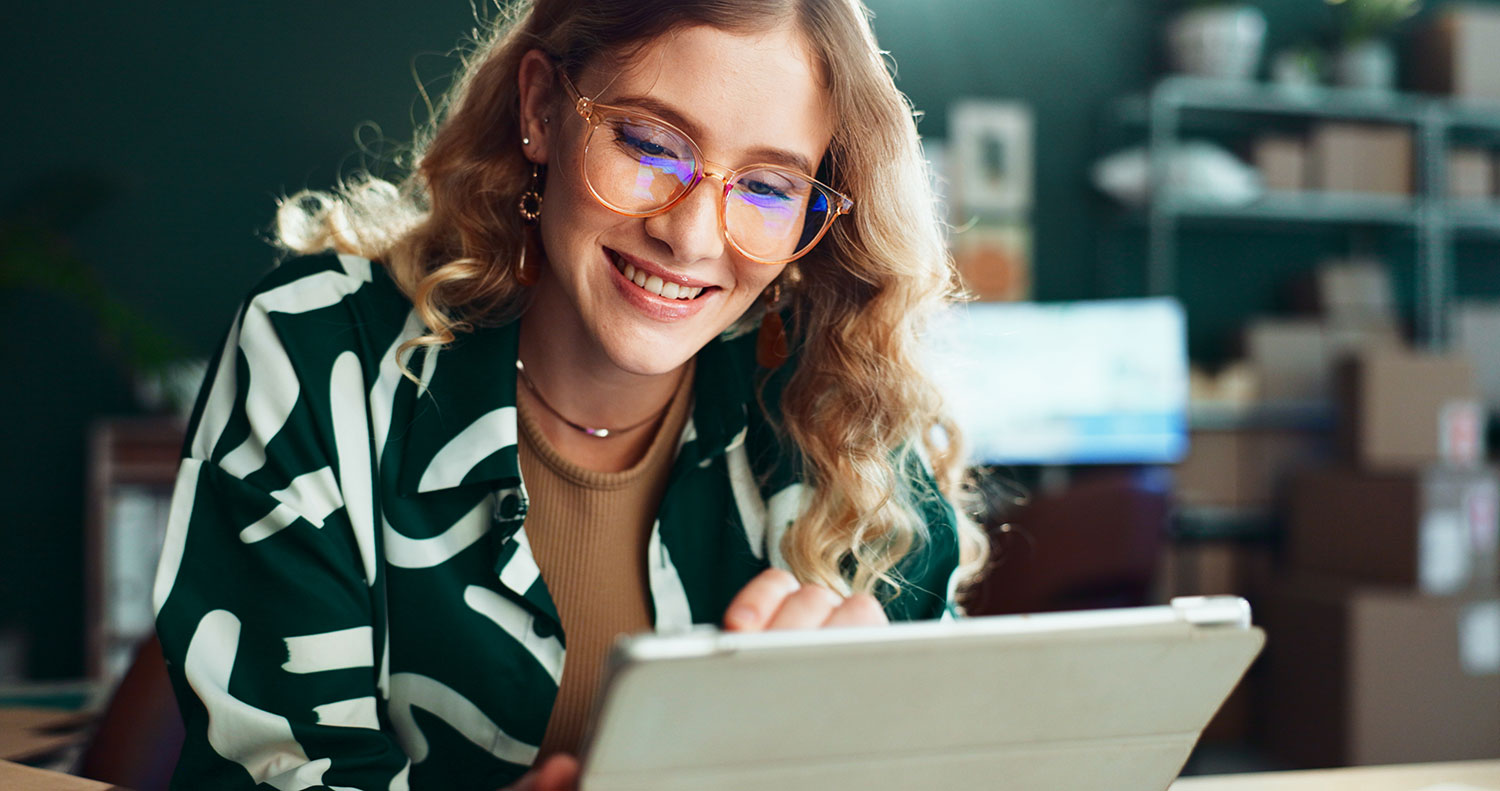 Smiling woman in glasses reading a message on her tablet in a small business workspace
